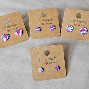 May include: Four cards with the text "Handmade with love" and different pairs of earrings. The earrings are made of polymer clay and feature a swirl pattern in pink, blue, and white. One pair is heart-shaped, one pair is square, and two pairs are round.