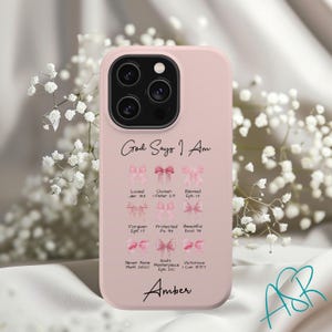May include: A pink phone case with a design that says "God Says I Am" and features pink bows with bible verses. The case also has the name "Amber" written at the bottom.