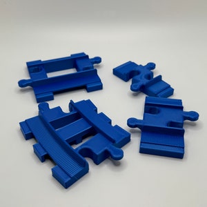 May include: Four blue plastic train track pieces. The pieces are designed to connect together to create a track for a toy train.