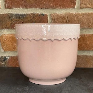 Può includere: Un vaso da fiori in ceramica rosa pallido con un bordo a festoni. Il vaso ha una glassa bianca sul bordo superiore.