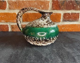 May include: A ceramic jug with a curved handle. The jug has a green band around the middle, with a speckled brown and white pattern above and below. The rim and handle are brown.