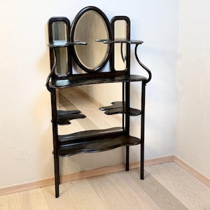 Puede incluir: Una estantería de pared de madera marrón oscuro con un espejo ovalado central flanqueado por dos espejos rectangulares verticales. La unidad incluye múltiples estantes curvos y asimétricos dispuestos a diferentes alturas, sostenidos por marcos de madera delgados.