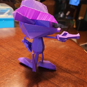 May include: A purple 3D printed figurine of a cartoon character with a large hat and a gun in its right hand.