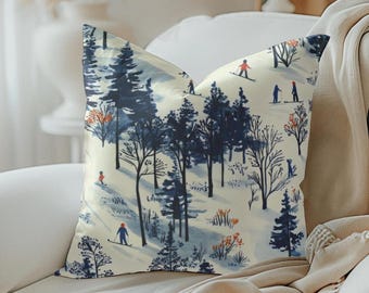 May include: A cream-colored throw pillow with a blue and white winter scene featuring skiers in a snowy forest. The pillow has a subtle watercolor effect.