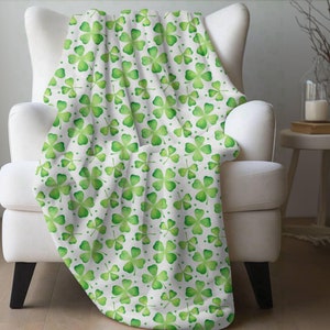 May include: White throw blanket with a green four-leaf clover pattern. The blanket is draped over a white armchair.