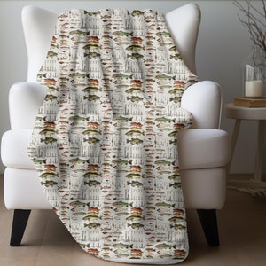 May include: A white throw blanket with a repeating pattern of colorful fish illustrations. The blanket is draped over a white armchair.