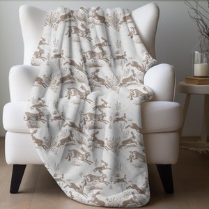 May include: A white throw blanket with a brown hare pattern. The blanket is draped over a white armchair.