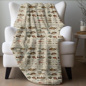May include: A cream-colored throw blanket with a vintage illustration of various fish species. The blanket features a detailed design with a light brown background and colorful fish illustrations.