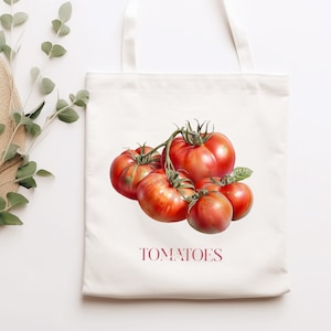 May include: A white canvas tote bag featuring a red and green illustration of tomatoes on a vine. The text "TOMATOES" is printed in pink below the illustration.