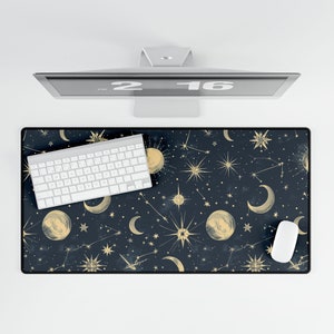 May include: A black desk mat with a gold celestial pattern featuring moons, stars, and constellations. A white keyboard and a white mouse are on the mat.