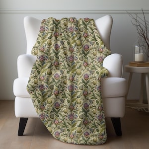 May include: A throw blanket draped over a white armchair. The blanket features a repeating floral pattern with thistle-like flowers in shades of purple, green, and tan. The background is a light beige.