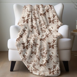 May include: A soft, plush throw blanket with a floral pattern featuring brown roses and leaves on a cream background.
