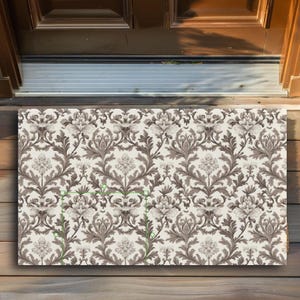 May include: A white doormat with a brown damask pattern. The pattern features intricate floral designs and swirling leaves.