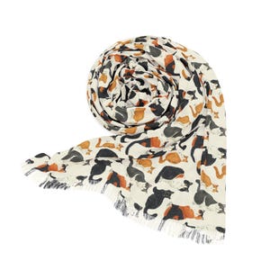 May include: A cream-colored scarf featuring a repeating pattern of various cats in shades of black, white, orange, and brown. The lightweight fabric is rolled into a circular shape and finished with delicate fringe along the bottom edge.