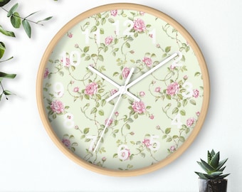 May include: A round, wooden framed clock with a white face and black hands. The clock face has a floral pattern with pink roses and green leaves on a light green background. The numbers 1 through 12 are printed in white on the clock face.