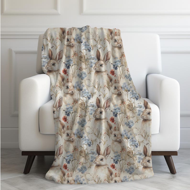 May include: A soft, plush throw blanket featuring a repeating pattern of watercolor bunnies and flowers in shades of blue, brown, and red.