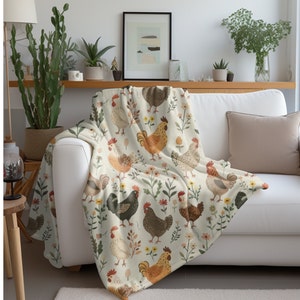 May include: A white throw blanket with a repeating pattern of colorful chickens and flowers. The chickens are brown, orange, and black with white accents. The flowers are pink, yellow, and green.