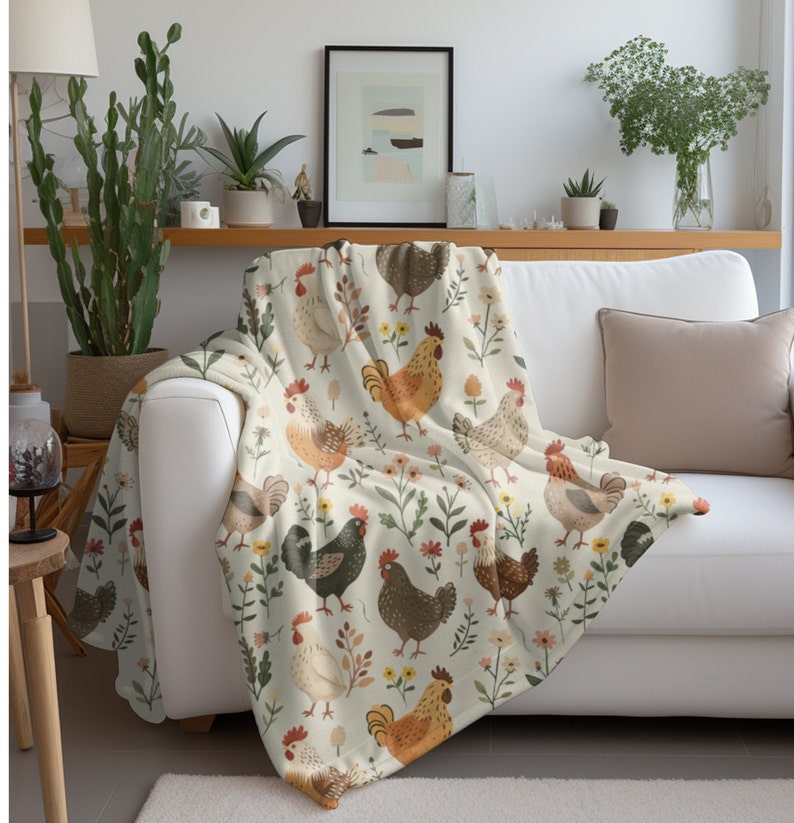 May include: A white throw blanket with a repeating pattern of colorful chickens and flowers. The chickens are brown, orange, and black with white accents. The flowers are pink, yellow, and green.