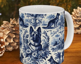 May include: White ceramic mug featuring a blue and white toile design with German Shepherd dogs, floral elements, and pastoral scenes. The mug has a white handle and a glossy finish, perfect for coffee or tea.