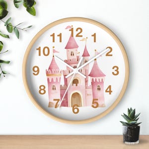 May include: A pink and white watercolor castle clock with gold numbers and hands. The clock has a wooden frame.