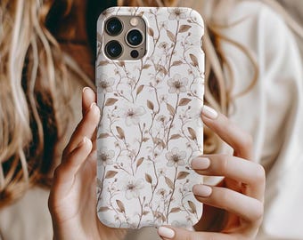 Könnte beinhalten: Eine weiße Handyhülle mit einem floralen Muster aus braunen Stielen und zarten weißen Blüten. Die Hülle wird in den Händen einer Person gehalten, wodurch die detaillierte Gestaltung und die Kamera des Telefons hervorgehoben werden.