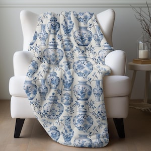 May include: A white throw blanket with a blue and white pattern of Chinese porcelain vases. The pattern is repeated throughout the blanket.