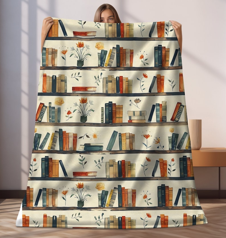 May include: A cream-colored throw blanket with a repeating pattern of bookshelves filled with colorful books and small floral arrangements. The bookshelves are brown with white shelves.