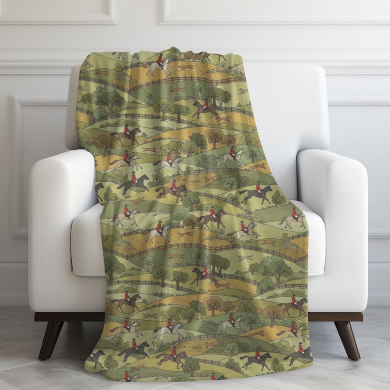 May include: A throw blanket draped over a white armchair. The blanket features a repeating pattern of riders on horseback, dressed in red coats, traversing a green and yellow landscape with trees and fences.