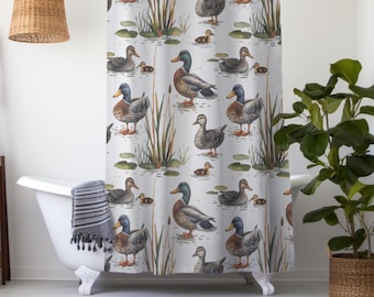 May include: A white shower curtain featuring a repeating pattern of ducks, ducklings, and aquatic plants. The ducks are depicted in various poses, with detailed plumage in shades of brown, gray, and blue. The curtain is hanging in a bathroom with a white bathtub and a woven basket.