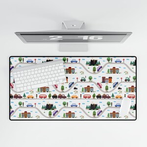May include: A white computer keyboard with a colorful city-themed mousepad featuring houses, cars, and trees. The mousepad has a white background with black outlines and a repeating pattern.