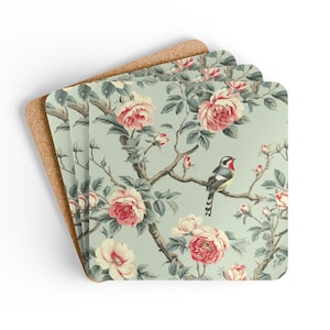 May include: Set of four square coasters with a floral design. The coasters feature a light blue background with pink roses, green leaves, and a bird perched on a branch. The edges are rounded, and the back is made of cork.