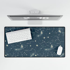 May include: A dark blue desk mat with a constellation pattern featuring white stars and gold lines. A white keyboard and mouse are on the mat.