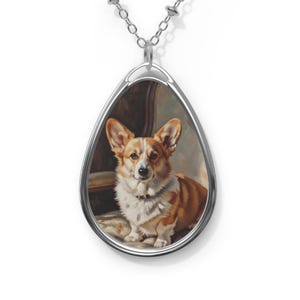 May include: Silver pendant necklace with a teardrop-shaped pendant. The pendant displays a painting of a Pembroke Welsh Corgi, with a white and reddish-brown coat, sitting on a cushion. The necklace has a delicate silver chain.
