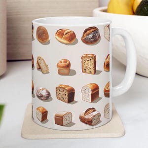 May include: White ceramic mug with a variety of bread illustrations printed on it. The mug has a handle on the right side.