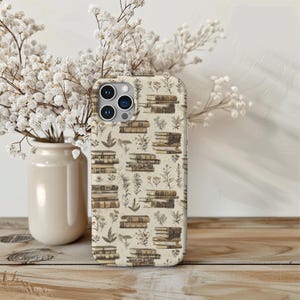 May include: A white iPhone case featuring a pattern of vintage books and botanical illustrations. The case has a cream background and displays a variety of brown and beige books stacked on top of each other. The botanical illustrations are in shades of brown and green.