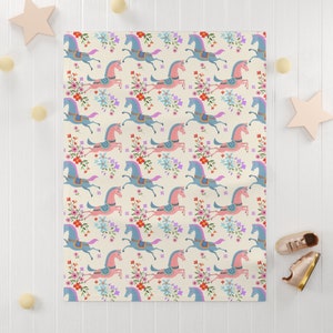 May include: A cream-colored fabric with a repeating pattern of pink and blue horses with floral accents. The horses are stylized and have a whimsical look.
