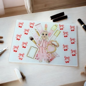 May include: A rectangular glass cutting board featuring a cartoon illustration of a woman in pink pajamas surrounded by makeup items. The board has a white background with pink bows and cherries.