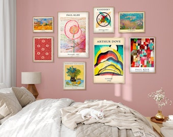 May include: A collection of framed art prints displayed on a pink wall above a bed. The prints feature various abstract and landscape paintings by artists like Paul Klee, Kandinsky, and Vincent van Gogh. The artwork includes a variety of colors and styles.