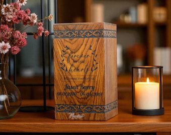 May include: A rectangular wooden cremation urn with a visible grain pattern, featuring engraved text that reads "forever in our hearts", "In loving memory of", "Jason Barry", and "01/01/1970 - 04/04/2019", with decorative carved borders.