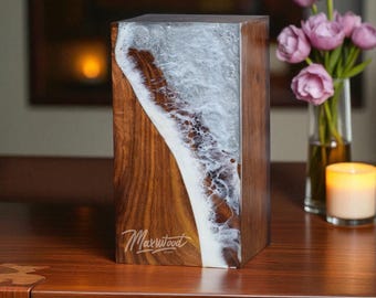 May include: A rectangular wooden block with a unique design. The block features a combination of dark wood and a white, swirling resin pattern, resembling ocean waves. The Maxwood logo is visible on the wood. The block is on a wooden surface.