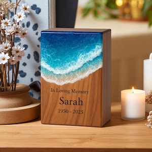 Könnte beinhalten: Gedenkurne aus Holz mit einem blau-weißen Ozeanwellen-Design auf der Oberseite. Auf der Vorderseite der Urne steht die Inschrift "In Loving Memory" über dem Namen "Sarah" und den Jahren "1950-2025".