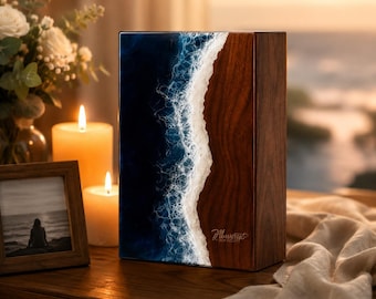 May include: A rectangular wooden urn featuring a dark brown wood grain on the right side and a blue resin ocean wave design with white foam on the left side. The text Always in our hearts is engraved in a cursive script on the wooden section.