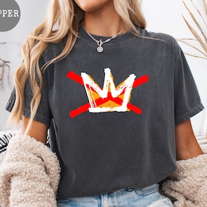 May include: Dark gray t-shirt featuring a graphic of a crown with red lines through it. The crown is white, yellow, and orange. The word "PEPPER" is in a gray circle in the upper left corner. The shirt is a casual style.