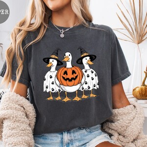 Peut inclure: T-shirt gris fonc&eacute; avec un motif d'Halloween. Le graphisme repr&eacute;sente trois canards, deux portant des chapeaux de sorci&egrave;re et des costumes de fant&ocirc;mes, et un en citrouille. Les canards sont regroup&eacute;s, cr&eacute;ant une image festive et fantaisiste.