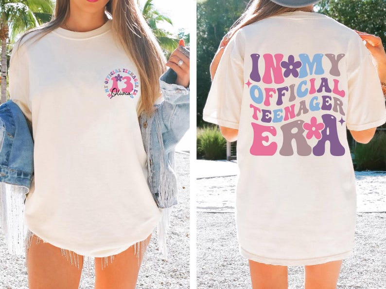 May include: A white t-shirt with a graphic on the front that says "In My Official Teenager Era" with flowers and a pink, blue, purple, and gray color scheme. The back of the shirt has a graphic that says "My Official Teenager Era" with a number 13 and a flower.