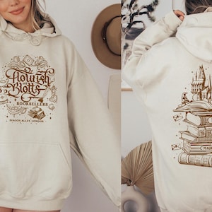 May include: A cream-colored hoodie with a brown graphic of the fictional bookstore "Flourish & Blotts" from the Harry Potter series. The text "Booksellers" is included in the graphic. The hoodie also features the text "Diagon Alley, London".