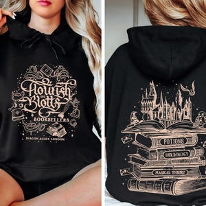 May include: Black hoodie with a gold graphic of the Hogwarts castle and a stack of books with the text "Potions", "Herbology", and "Magical Theory" on the back. The front of the hoodie has a gold graphic of the text "Flourish & Blotts Booksellers Diagon Alley London".
