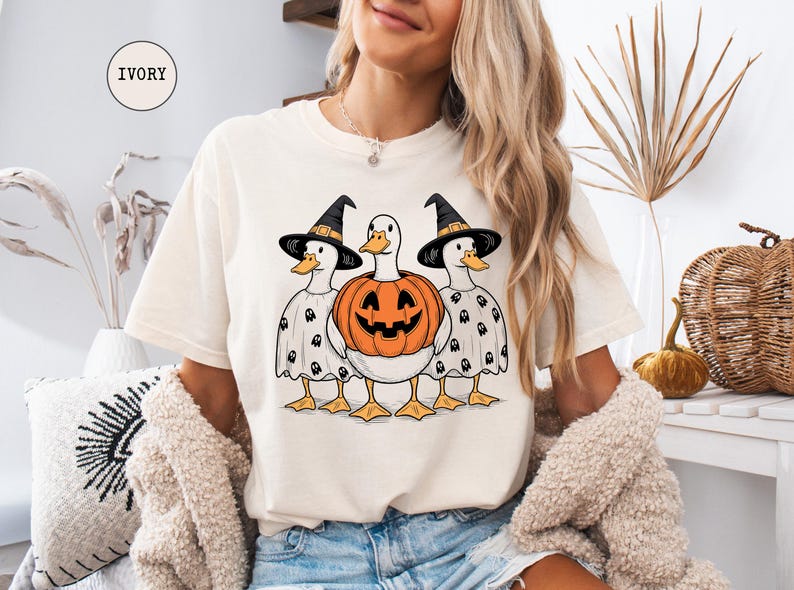 Peut inclure: T-shirt ivoire avec un motif d'Halloween. Le motif repr&eacute;sente trois canards, deux portant des chapeaux de sorci&egrave;re et des costumes de fant&ocirc;mes, et un tenant une citrouille sculpt&eacute;e. Le t-shirt est de coupe d&eacute;contract&eacute;e.