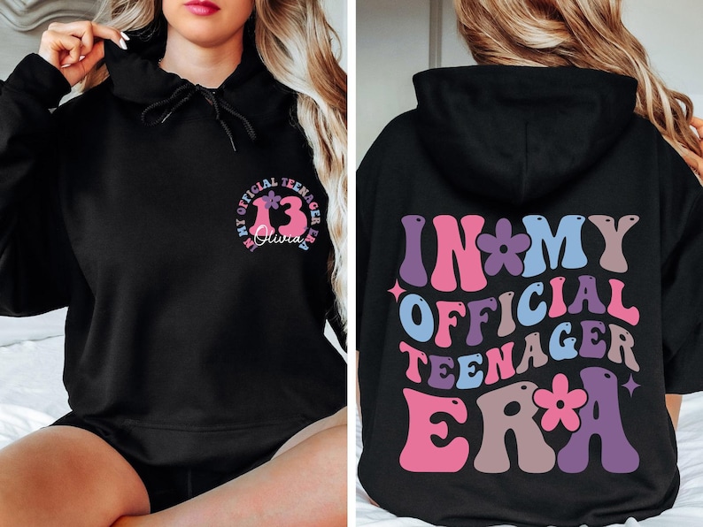 May include: Black hoodie with the text "In My Official Teenager Era" in colorful, retro-style letters with flowers on the back. The front of the hoodie has a circle with the number "13" and the text "My Official Teenager Era" in smaller letters.