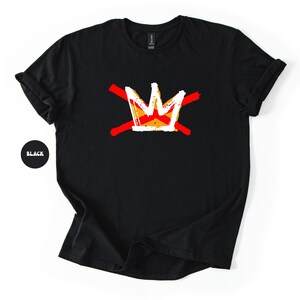 May include: Black t-shirt featuring a white and orange crown design crossed by two red lines. The crown has a yellow and orange center. The shirt is made of a soft material and has a crew neck.